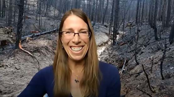 a woman in front of a burnt forest