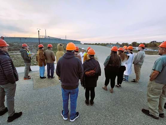 Adult tour attendees stand near a tour guide, outside at the Water Treatment Facility.