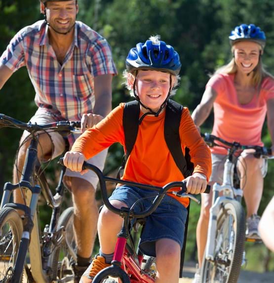 A child and parents ride on bikes with helmets.