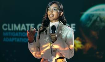 A woman speaking on a conference stage, holding a microphone.