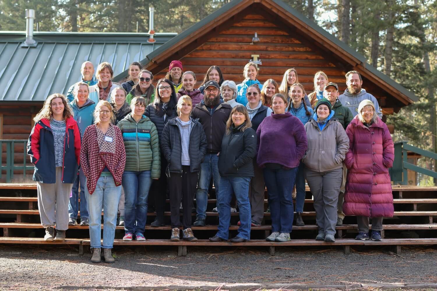 Group Photo of all participants from 2023 Educator Workshop standing in front of a log cabin.