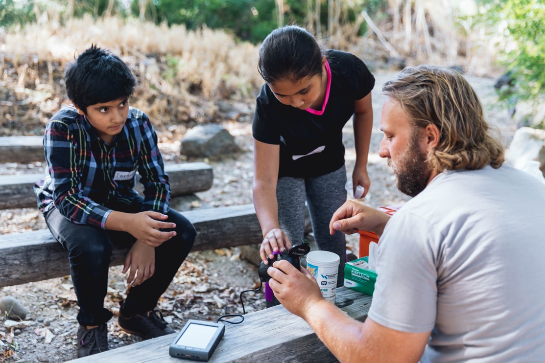 Two children observing a field scientist's work.