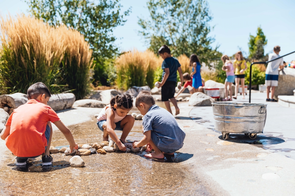 Children playing in The WaterShed's simulated river. Three children in the foreground are arranging rocks to alter the flow of warer.