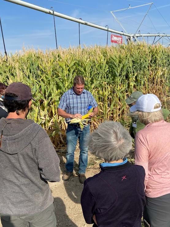 In an agricultural field, an instructor is giving a demonstration to a group of adult students in the Master Naturalist Program