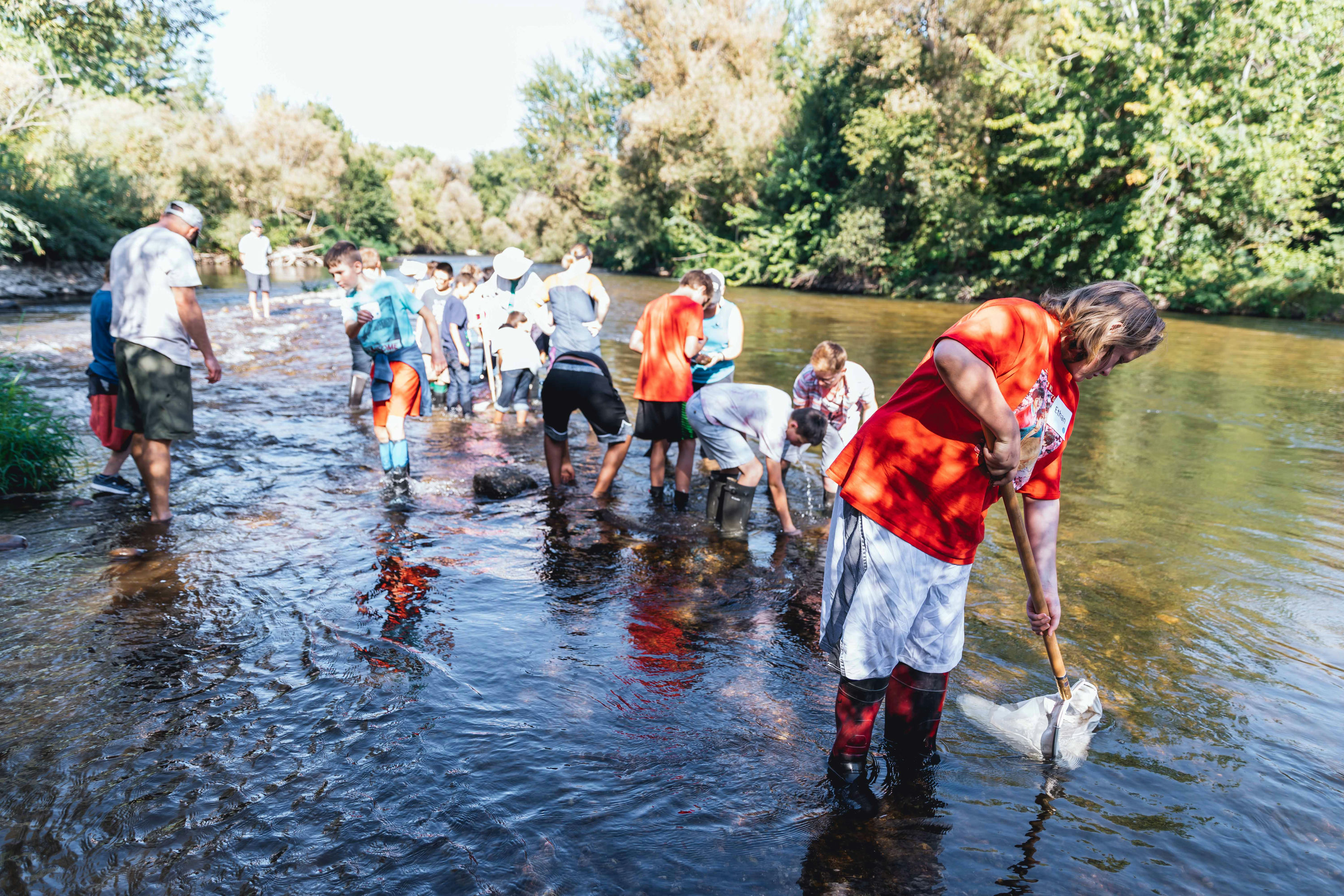 A group of students and adult leaders wade in the Boise River collecting and observing samples.