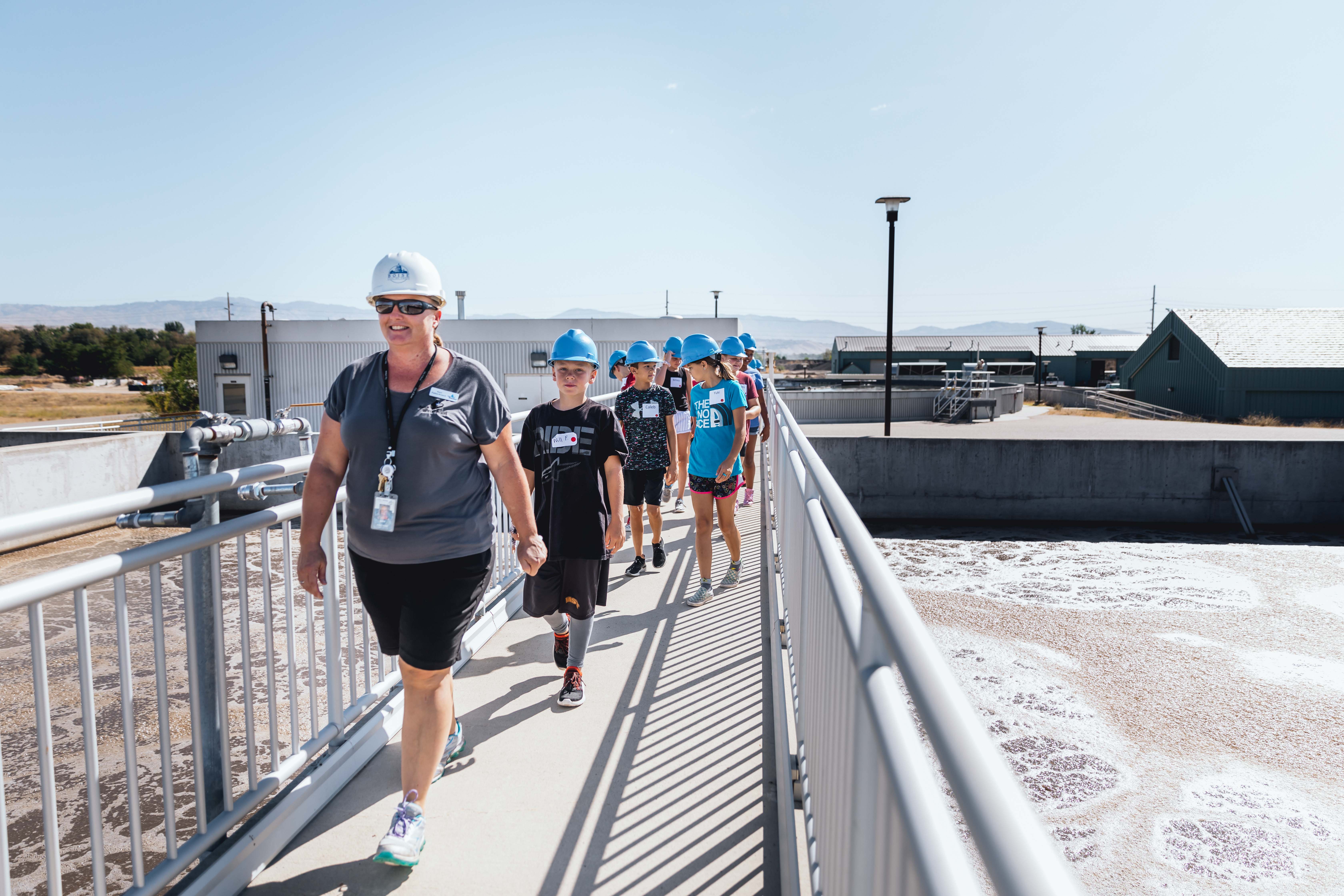 A group of children on a tour walk across a catwalk over a water reservoir.